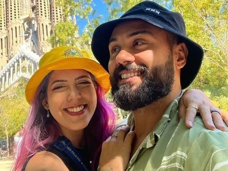 Ein lächelndes Paar mit Hüten posiert vor der Sagrada Familia in Barcelona.